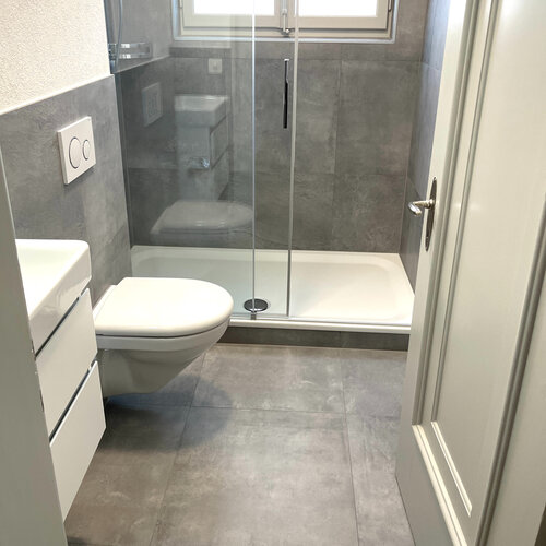 Dusche in einer Mietwohnung im schönen Monbojou Quartier in Bern. Dusche mit modernen Keramik in Betonoptik grau und weissen Sanitärmöbeln.