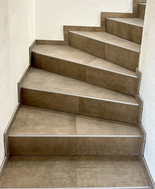 Gewundene Treppe mit brauen Feinsteinzeugplatten verkleidet und passendem Sockel