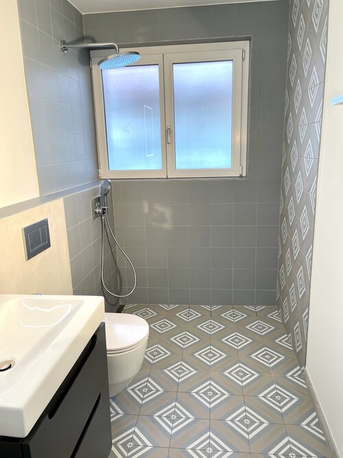 Badezimmer im Jugensstyle mit schönen hellblauen Fliesen. Der Boden hat ein geometrisches Muster und ist mit der gleichen Farbe in Uni kombiniert. Die neuen dunklen Möbel wirken harmonisch dazu.