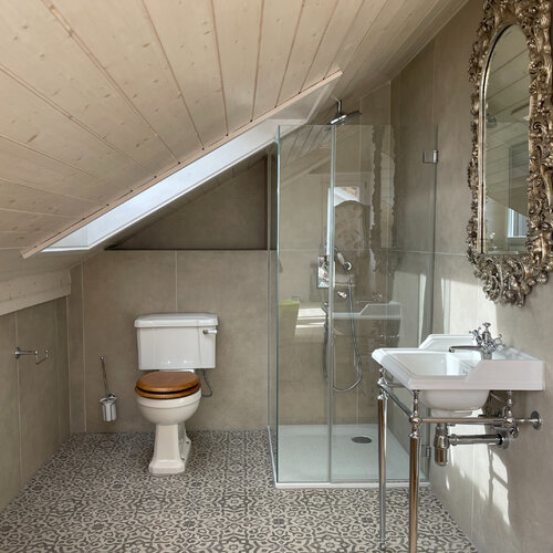 Badezimmer mit Dekorboden und Grossformat an den Wände in einem Taupe Ton. Passend dazu gehören Sanitärarmaturen im englischen Design.