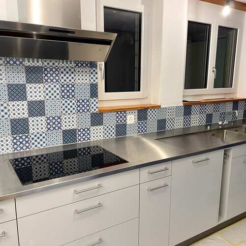 Küchenrückwand mit handgemachten Wandfliesen. Der Dekormix in blau passt wunderbar zu der Chromstahlabdeckung und den weissen Schränken.