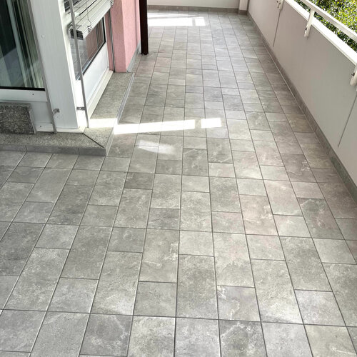 Schöner Keramik Balkonboden mit grauen Platten in mehreren Formaten passend zu rosa Hausfassade.