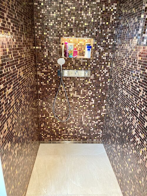 Duschecke mit Glasmosaik Mix in braun glitzernd Farben und Goldmosaik. Ausgefugt mit einer Goldsplitterfuge schimmert die Dusche noch mehr und die beleuchtete In-Box erhellt es zusätzlich.